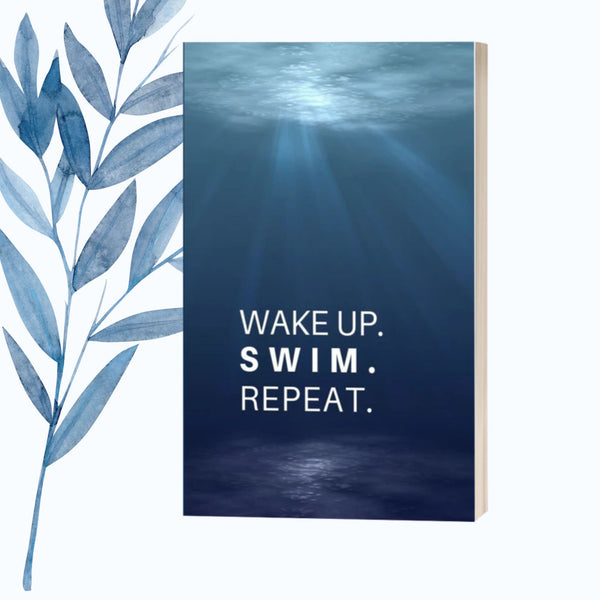 A notebook featuring the phrase "Wake Up. Swim. Repeat." on a sleek, glossy cover.